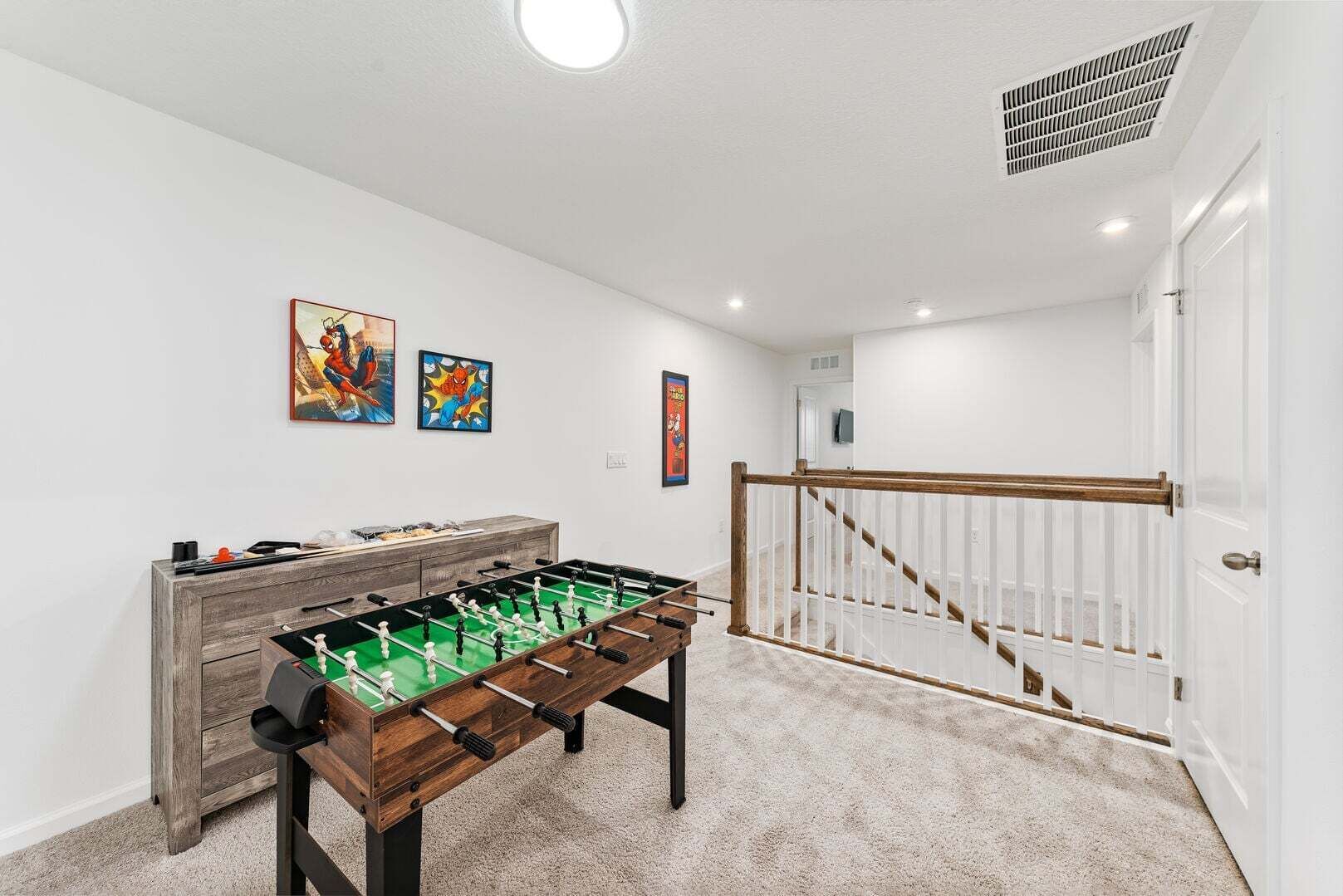 Une pièce avec une table de baby-foot, un meuble en bois et un escalier muni d’une rampe.