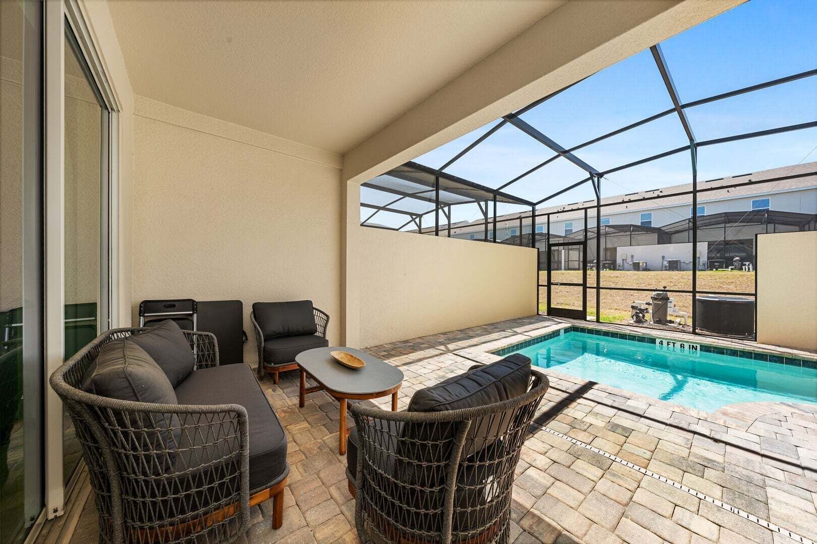 A covered outdoor area with a pool, wicker furniture, and a view of a building.