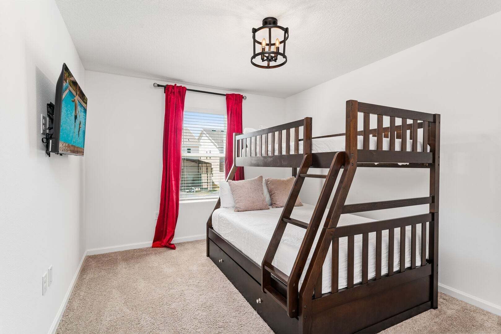 A bunk bed with a wooden frame, a window with red curtains, and a wall-mounted light fixture.