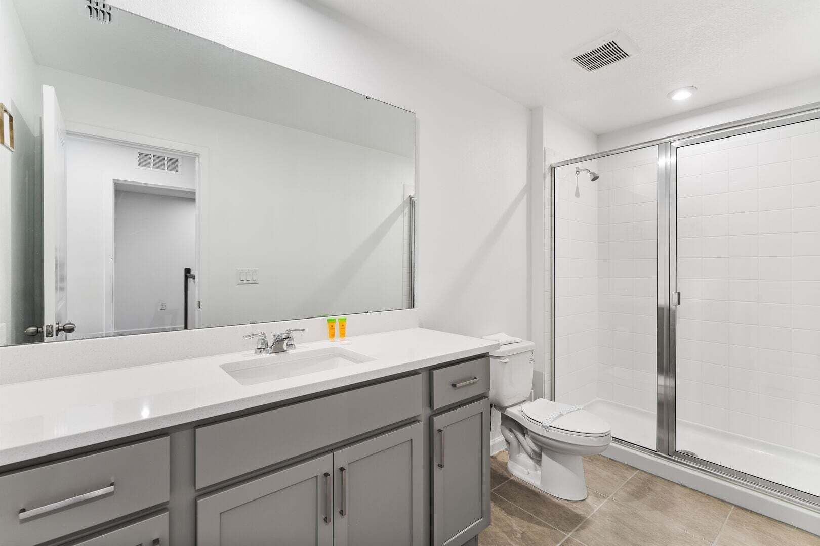 Ein modernes Badezimmer mit großem Spiegel, Waschbecken, Toilette und einer Duschkabine aus Glas.