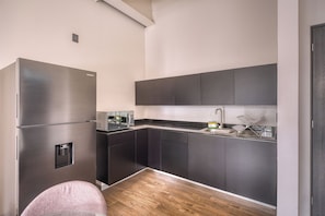 Una cocina moderna con un refrigerador de acero inoxidable, armarios oscuros, piso de madera y microondas integrado.