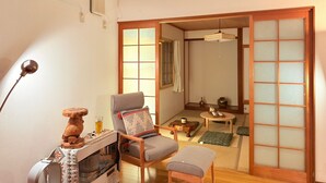 A traditional Japanese room with tatami flooring, a low wooden table, a cushioned chair, and a sliding shoji screen. - Sol Stay | Patchwork Road Lavender Summer | Blue Pond & Shirogane Hot Springs (20 minutes) | Detached House in the City with Garage (美瑛町)