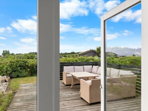 A balcony with wicker furniture, a wooden deck, and a view of a rural landscape.