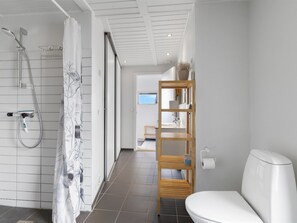 A modern bathroom with a shower, toilet, and a wooden shelf unit.