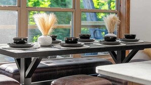 Un tavolo da pranzo con ciotole nere e un vaso bianco con piante secche, con vista sulla vegetazione attraverso una finestra.