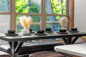 A dining table with black bowls and a white vase with dried plants, set against a window with a view of greenery. - New • Luxury • Location • Theater • 4decks • Views (Gatlinburg)