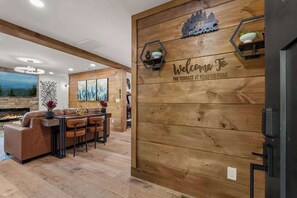 A modern living room with a fireplace, a wooden wall with a welcome sign, and a dining area with a sofa and chairs. - New • Luxury • Location • Theater • 4decks • Views (Gatlinburg)