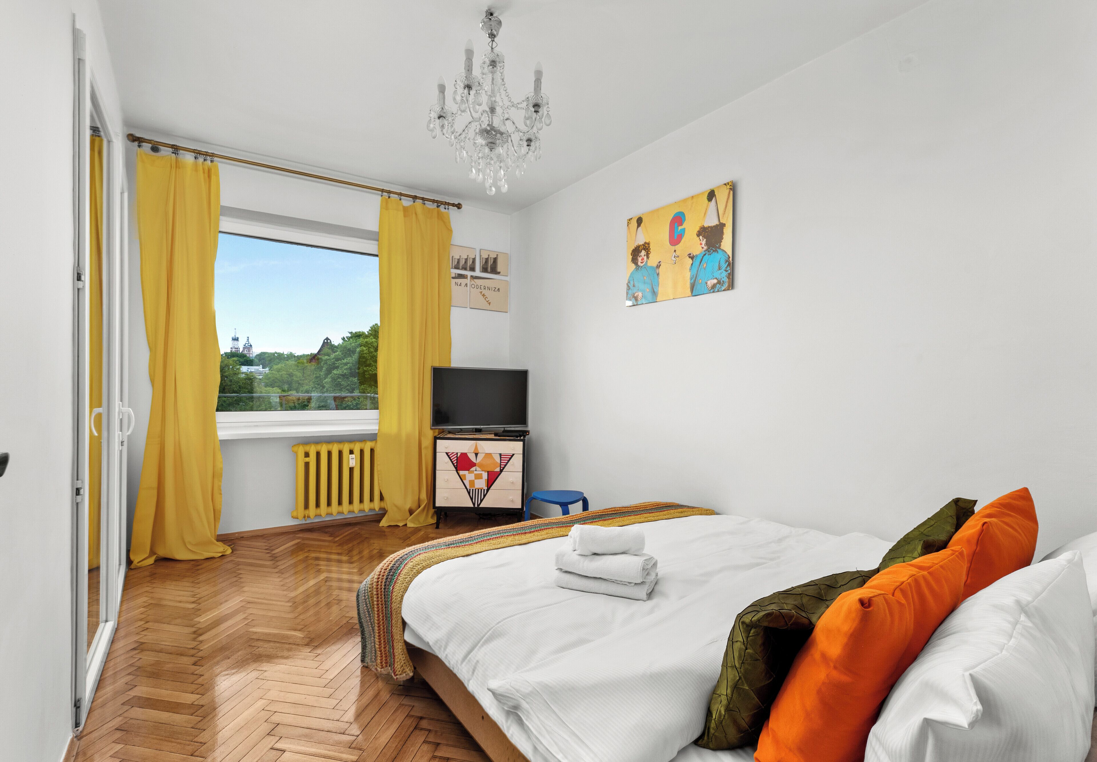 Een slaapkamer met een bed, een televisie, een radiator, een raam met gordijnen en een schilderij aan de muur.