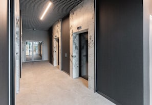 Un couloir moderne doté d’ascenseurs, d’un sol carrelé et d’un plafond orné d’un motif en réseau.