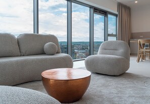 A modern living room with a large window, a sofa, a chair, and a round coffee table. - Olszynki Park Superior Apartment (Rzeszów)