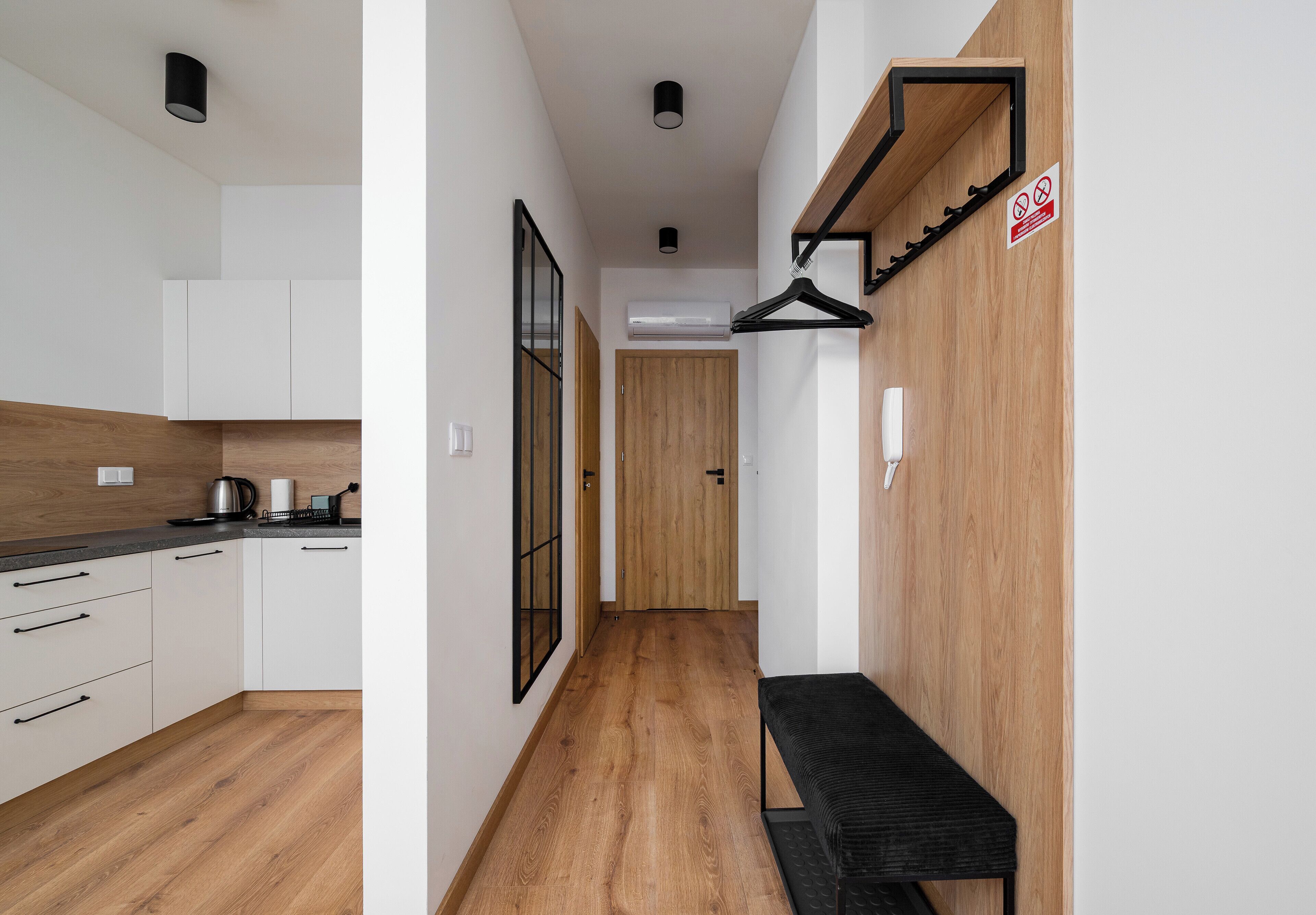 A modern kitchen with white cabinets, a wooden floor, and a black bench.