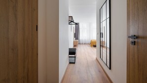 Un couloir avec un plancher en bois, un banc, un lit recouvert d’une couverture jaune et un grand miroir accroché au mur.