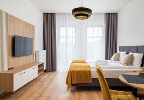 Ein modernes Hotelzimmer mit Bett, Schreibtisch, Fernseher und einem Fenster mit Vorhängen.