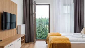 Una moderna camera d'albergo con una scrivania in legno, una televisione a schermo piatto, un letto con coperta gialla e un balcone con vista sugli alberi.