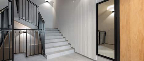 Una escalera con barandilla negra, paredes blancas y una puerta de madera.