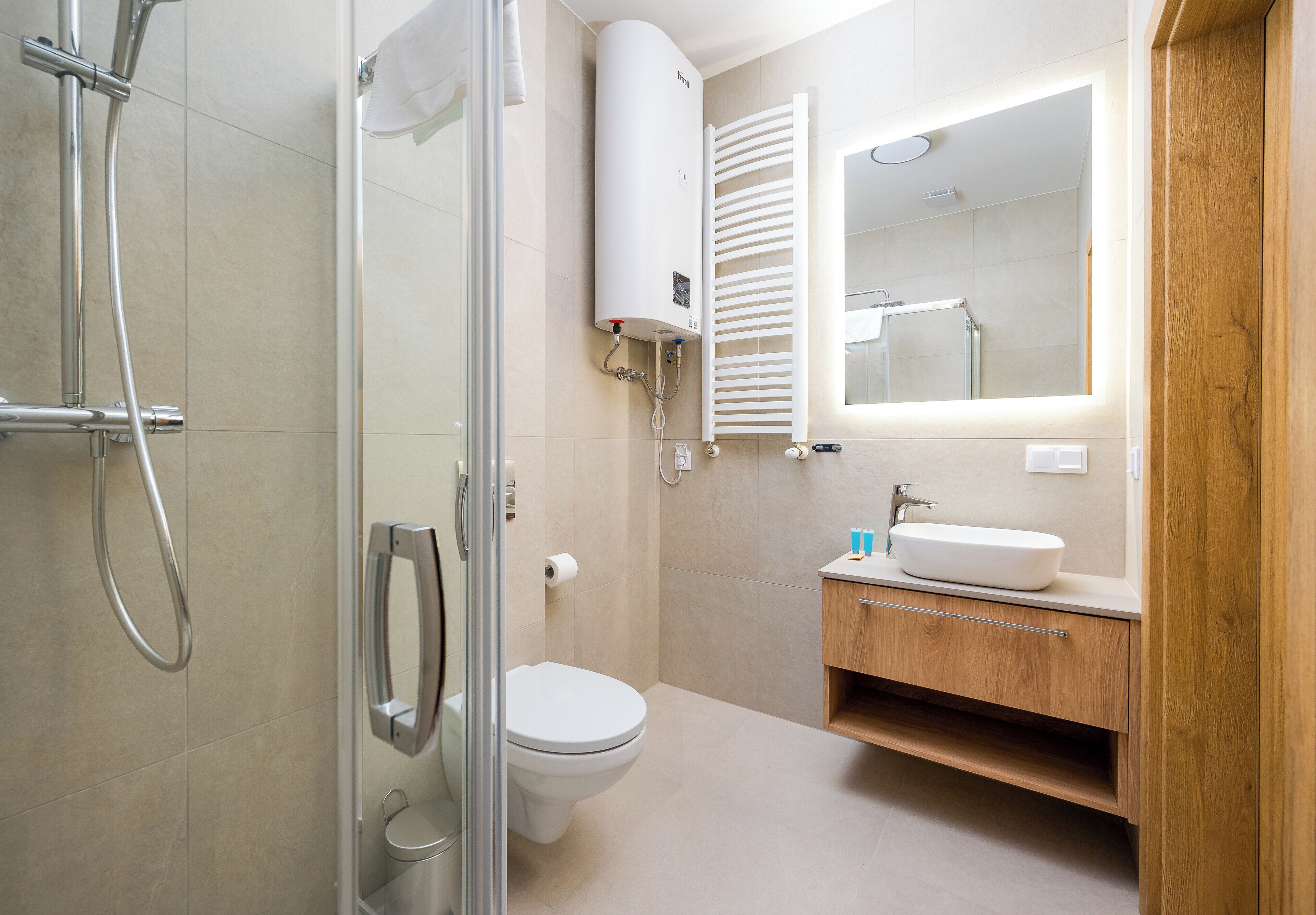 Un bagno moderno con box doccia in vetro, un water, un lavabo con mobile contenitore in legno e un riscaldatore a parete.