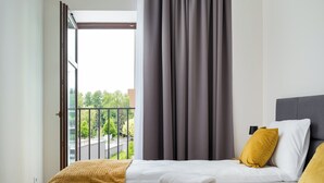 Et hotelværelse med seng, et vindue med gardiner, balkonudsigt og et natbord med lampe.