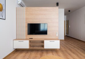 Ein modernes Wohnzimmer mit Flachbildfernseher an einer Holzwandanlage, einem weißen Sofa und Holzboden.
