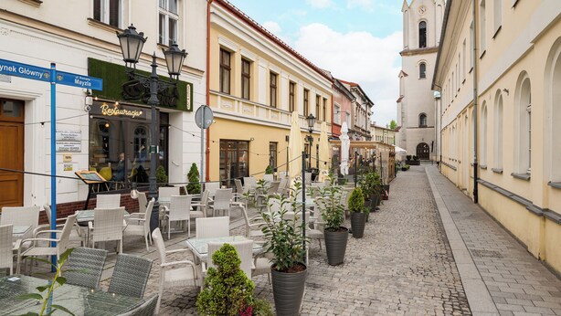 Une rue pavée avec des terrasses, une église et des bâtiments portant des enseignes.
