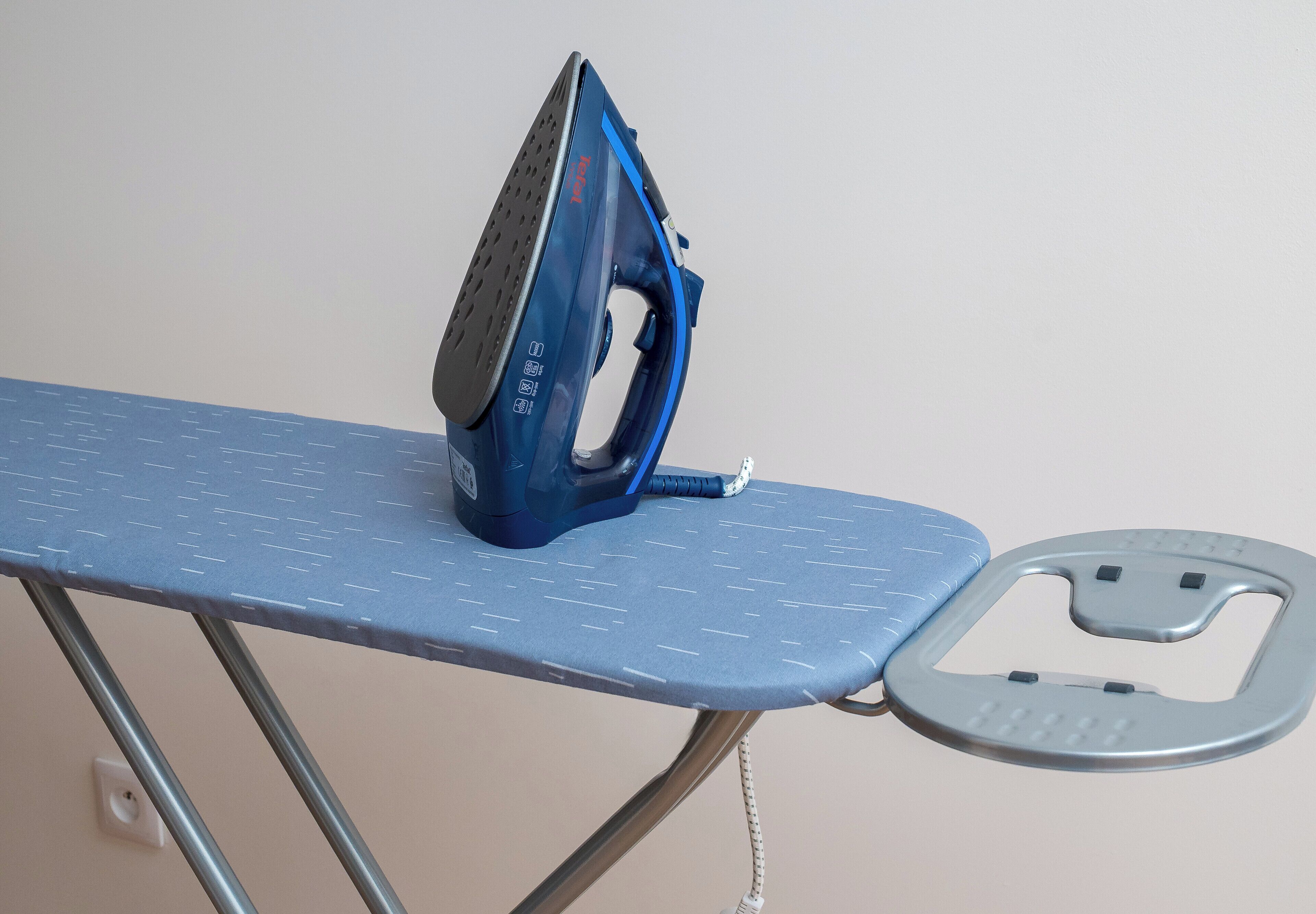 Ein blaues Bügeleisen auf einem blauen Bügelbrett mit Fußpedal.