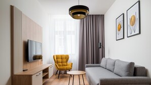 Un salon moderne avec un canapé, un fauteuil jaune, un téléviseur et des œuvres d’art accrochées au mur.
