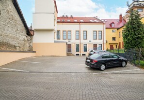 A parking area with a black car, a building with a red roof, and a tree.
