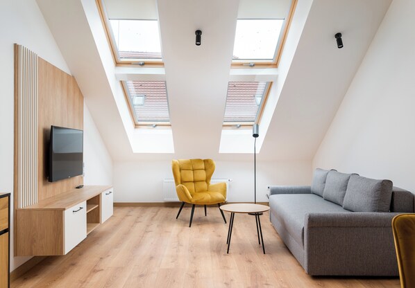 A modern loft bedroom with skylights, a sofa, a yellow armchair, and a TV.