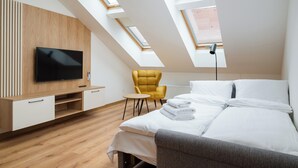 Ein modernes Schlafzimmer mit Fernseher, einem Bett, einem gelben Sessel und Dachfenstern.