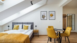 Een moderne slaapkamer met dakraam, een bed met een gele deken, een nachtkastje met een lamp en een eethoek met gele stoelen.