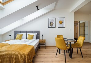Ein modernes Schlafzimmer mit Dachfenster, einem Bett mit gelber Decke, einem Nachttisch mit Lampe und einem Essbereich mit gelben Stühlen.
