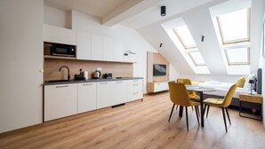 Een moderne keuken met witte kasten, een magnetron en een eethoek met gele stoelen.