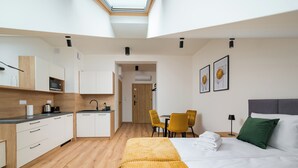 Una habitación de hotel moderna con cama, escritorio, silla, mesa de comedor y kitchenette.