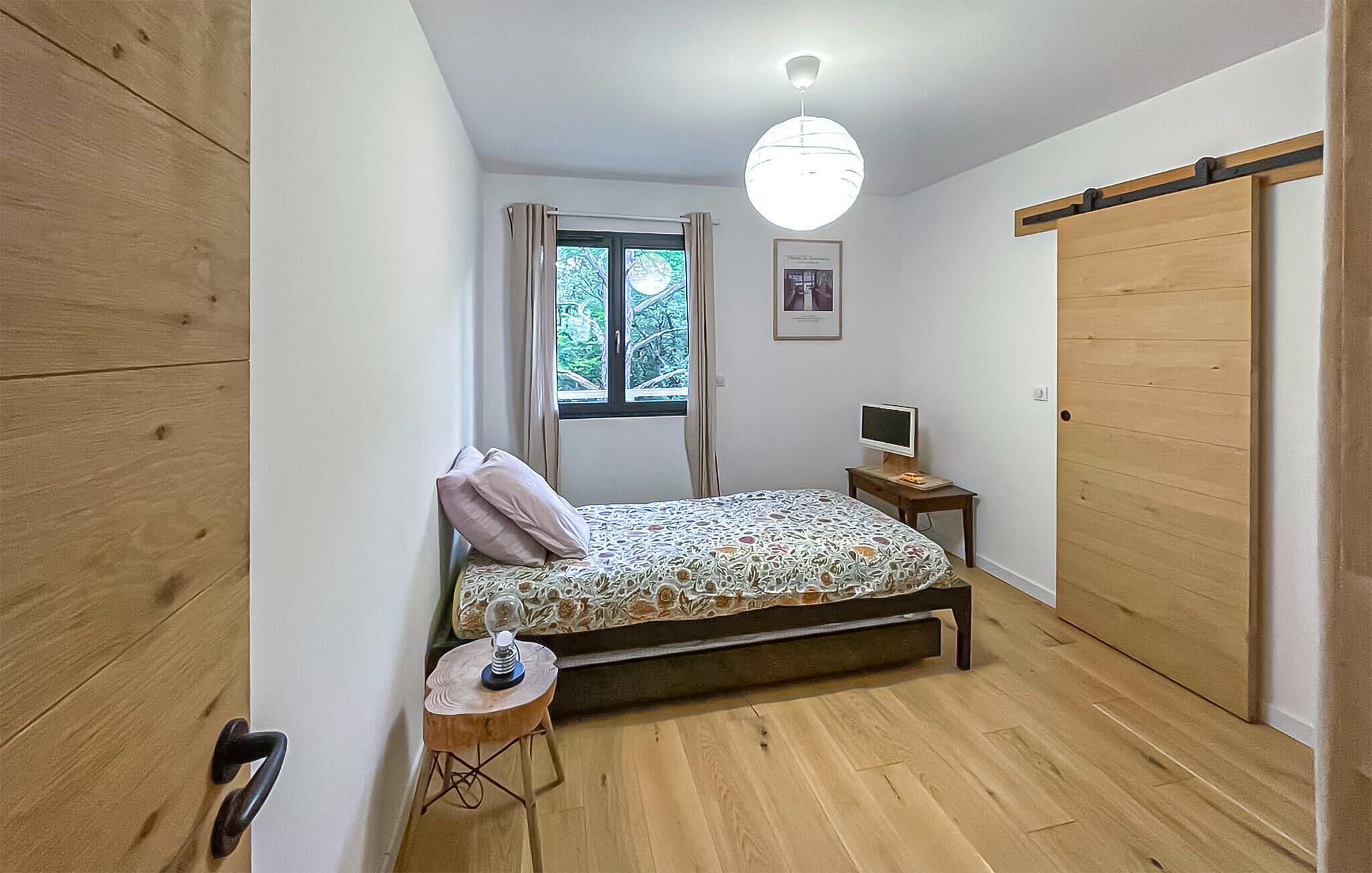 Een slaapkamer met een bed, nachtkastje met lamp, televisie, raam met gordijnen en een kledingkast.