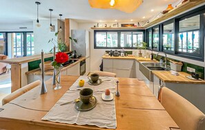 Eine moderne Küche mit Holzausziehtischen, einem Esstisch gedeckt mit Teetassen und großen Fenstern, die für natürliches Licht sorgen.
