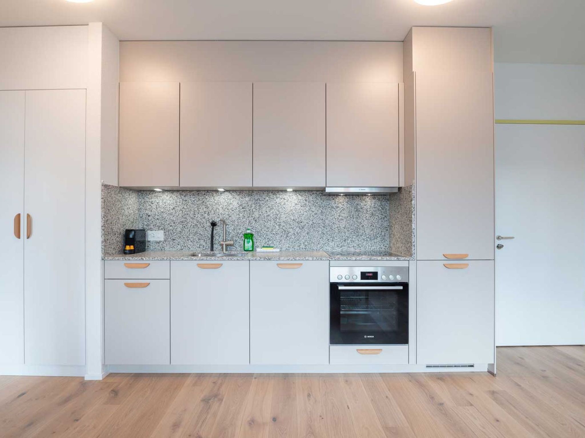 A modern kitchen with light-colored cabinets, a granite countertop, and a Bosch oven.