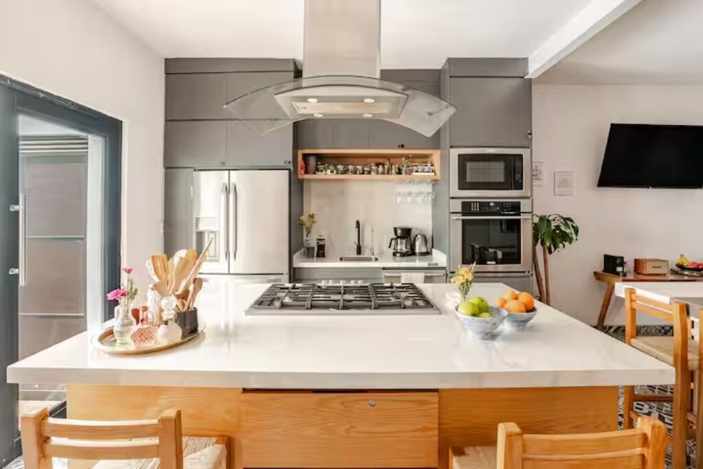 Une cuisine moderne dotée d’un îlot central, d’appareils électroménagers intégrés et d’un téléviseur à écran plat fixé au mur.