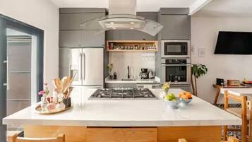 Une cuisine moderne dotée d’un îlot central, d’appareils électroménagers intégrés et d’un téléviseur à écran plat fixé au mur.