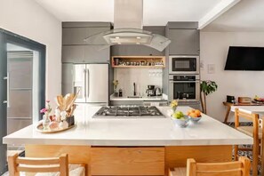 Une cuisine moderne dotée d’un îlot central, d’appareils électroménagers intégrés et d’un téléviseur à écran plat fixé au mur.