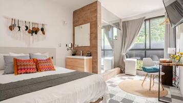 A bedroom with a bed, bedside table, mirror, and a view of the outdoors.