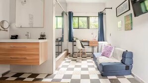 A compact room with a checkered floor, a desk, a sofa, a mirror, and a TV.