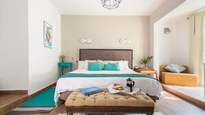 A bedroom with a bed, a bedside table, a chair, a bench, and a wall-mounted light fixture.