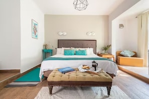 A bedroom with a bed, a bedside table, a chair, a bench, and a wall-mounted light fixture.