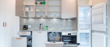 A modern kitchen with white cabinetry, a built-in oven, a dishwasher, and a refrigerator.