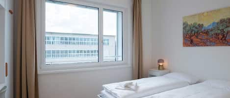 A hotel room with two beds, a window, a painting, and a nightstand with a lamp.