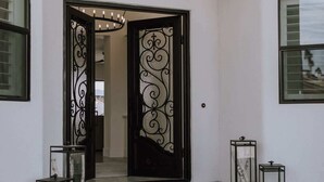 Un pasillo interior con una puerta negra ornamentada, una lámpara colgante y cuadros en las paredes.