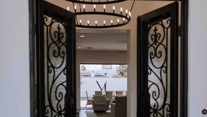 Una puerta con intrincados detalles en hierro negro, un felpudo con la palabra 'WELCOME' y una vista a un salón con sofá y alfombra.