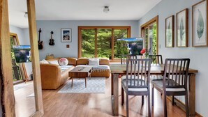 A living room with a sofa, coffee table, dining table, chairs, and a TV. - Secluded North Cascades Retreat | Private Trail + Fire Pit (Marblemount)