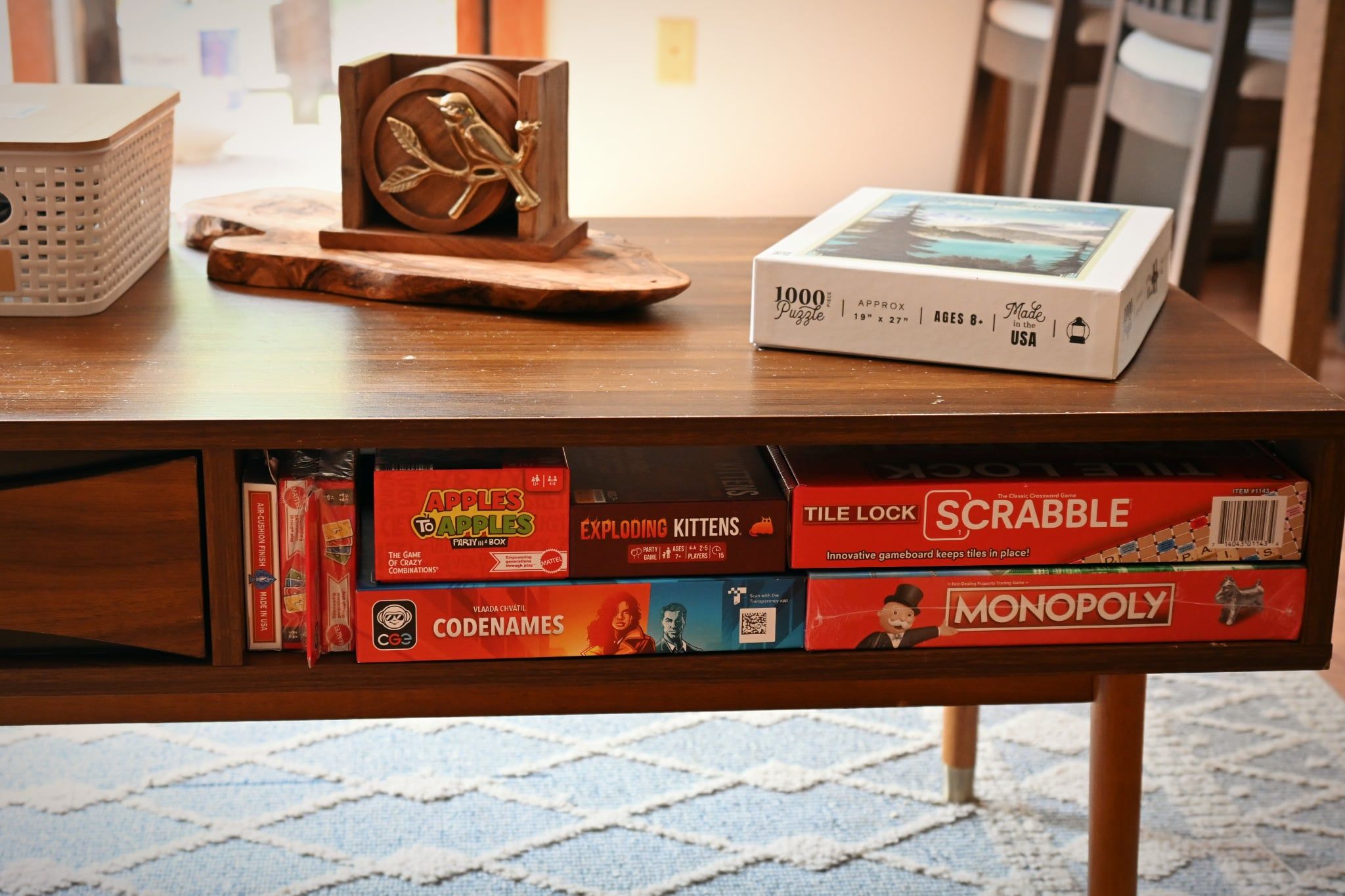 Una mesa de madera con varios juegos de mesa, incluyendo Scrabble y Monopoly, y una caja de rompecabezas.