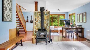 A living room with a stone fireplace, wooden furniture, a staircase, and a dining area with chairs and a table. - Secluded North Cascades Retreat | Private Trail + Fire Pit (Marblemount)