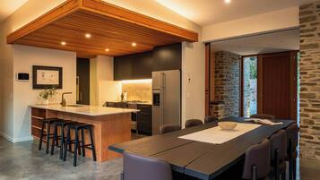 Une cuisine moderne dotée d’un îlot central, d’un coin repas avec une longue table et d’un mur en pierre.